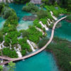 Waterfalls in Plitvice National Park. Aerial view. One lake flows into another surrounded by lush vegetation. Water has natural vivid turquoise color. Popular touristic attraction.